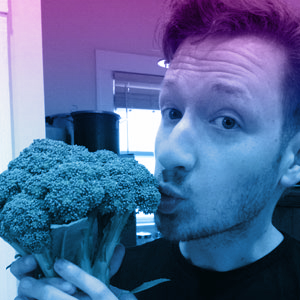 Indoor photo of Nick O'Neill holding and kissing a stem of broccoli